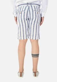 Pantaloni shorts in lino a righe blu e bianche con vita regolabile, dotati di due tasche posteriori e un tatuaggio visibile sulla parte inferiore della gamba.