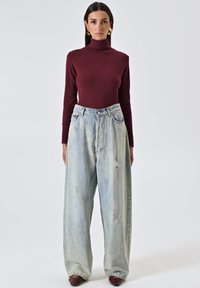 Bordeaux turtleneck top gecombineerd met oversized lichtblauwe versleten spijkerbroek. Losse pasvorm met zichtbare stiksels en subtiele vervaging.