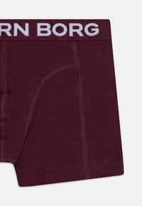 Burgundi színű boxer alsó, fehér elasztikus derékkal, melyen a "BORN BORG" felirat található, sima szövetből készült, testhezálló fazon, varrási részletekkel.