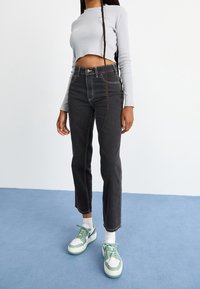 Top corto de manga larga gris, jeans negros de tiro alto y zapatillas blancas-verdes con cordones. El material parece suave con ligeras variaciones de textura.