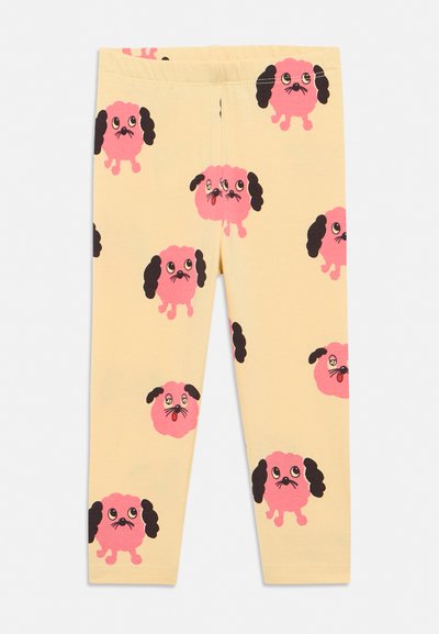 Bézs színű gyermek leggings, amelyeket ismétlődő rózsaszín rajzfilmes kutyafejek mintáznak, fekete fülekkel és kifejező szemekkel.