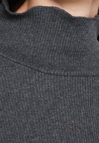 Maglione a collo alto in maglia a coste grigio scuro con leggero arricciamento del tessuto sul bordo superiore, che mostra parte di un collo e di un mento.