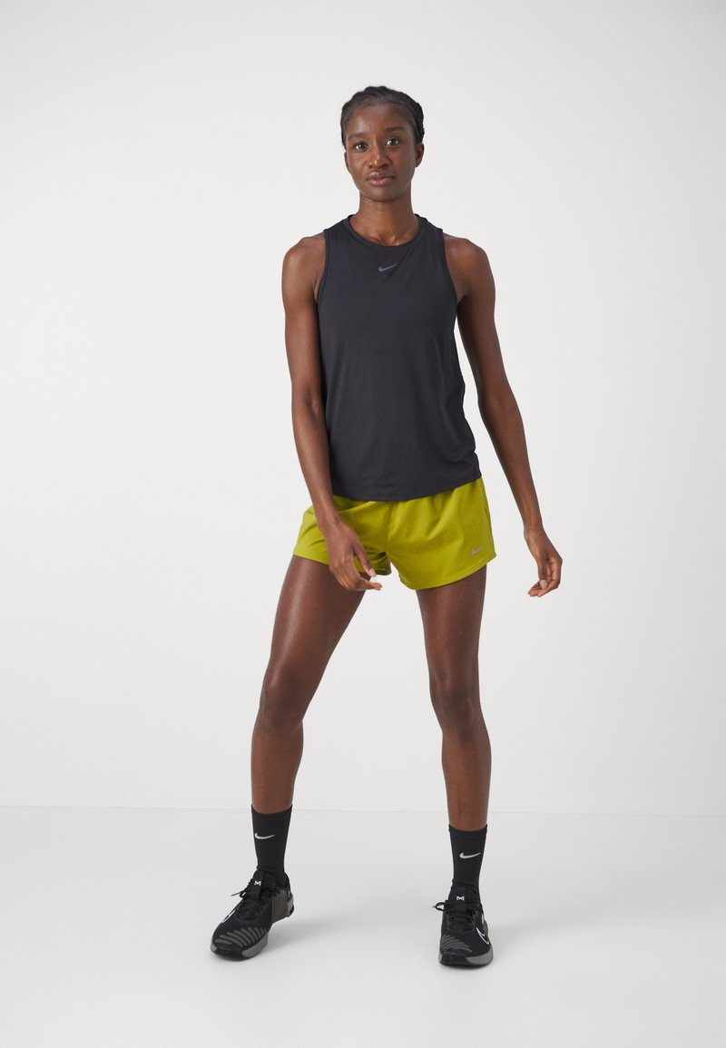 Schwarzes ärmelloses Sportoberteil, leuchtend grüne Shorts, schwarze Socken und schwarze Schuhe. Einfaches Design und leichte Materialien, die für den Sport geeignet sind.