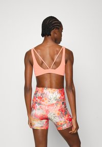 Sutia desportivo cor-de-rosa claro com alças cruzadas nas costas, combinado com calções de cintura alta com padrão floral multicolorido. Textura de tecido suave.