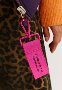 Jasnoróżowa metka z czarnym tekstem przypięta do suwaka. Tekst brzmi: "To doskonały dzień, aby zrobić coś, co kochasz." Tło w panterkę.