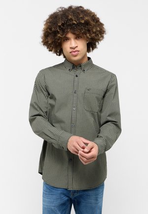 Green and black checked button-up shirt with a collar, long sleeves, and a front pocket, made from a smooth fabric. Worn over blue jeans.