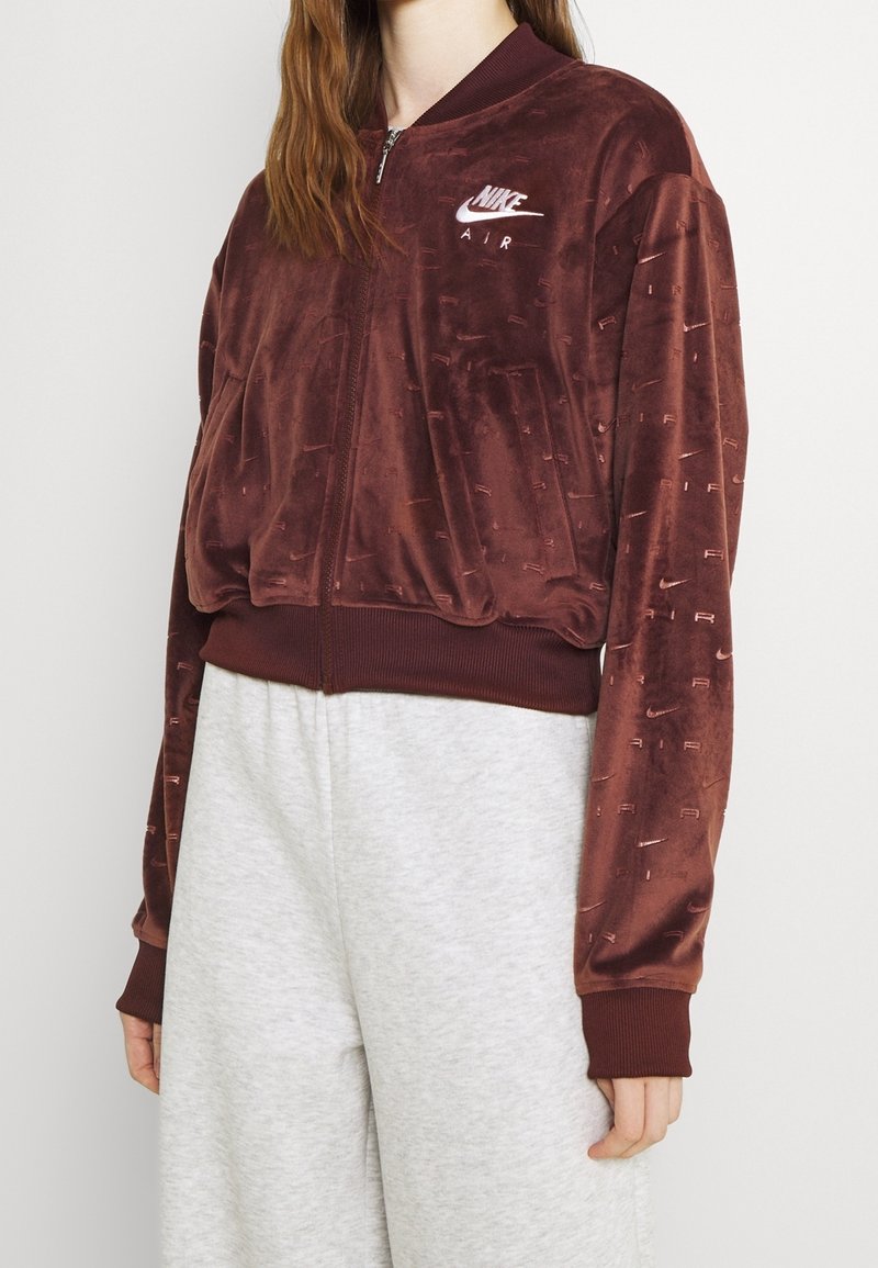 Burgundská bomber bunda na zip z jemného sametu s žebrovanými manžetami a lemem. Vybavena malým logem Nike na hrudi a hladkým, jemným povrchem.
