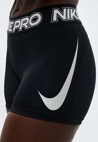 Κοντινό πλάνο ενός ατόμου που φοράει μαύρα συμπιεστικά σορτς Nike Pro με μεγάλο λευκό λογότυπο Nike στο μηρό και λογότυπο στη μέση.