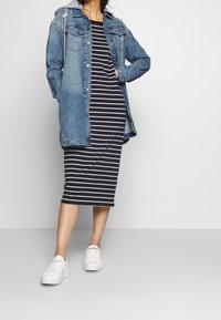 Veste en jean à délavage clair, fermeture à boutons à l'avant et capuche. Robe midi à rayures noires et blanches. Baskets blanches.