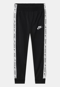 Pantalones deportivos negros hechos de una tela elástica, con una cinturilla elástica, puños en los bajos y franjas laterales blancas con la marca "NIKE".