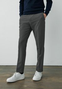 Pantalones grises ajustados hechos de una tela suave, con un diseño de pierna recta y una textura sutil, combinados con zapatillas blancas.