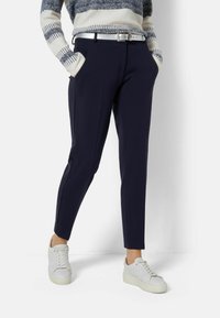 Marinblå byxor med slim fit, sidofickor och en subtil pressveck, kombinerat med vita sneakers och en stickad randig tröja.