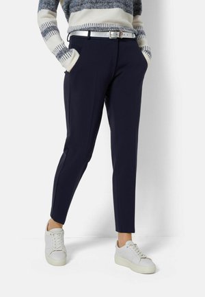 Pantalon navy slim fit, avec poches latérales et un pli subtil, associé à des baskets blanches et un pull en tricot rayé.