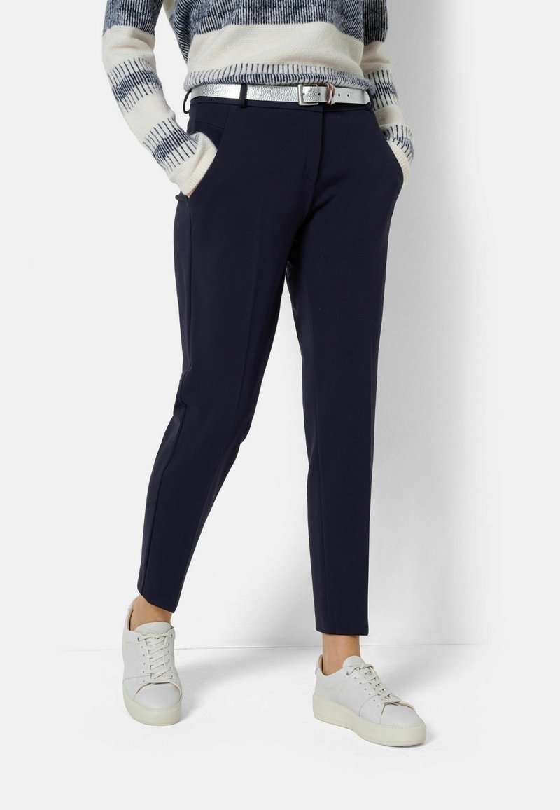 Marinblå byxor med slim fit, sidofickor och en subtil pressveck, kombinerat med vita sneakers och en stickad randig tröja.