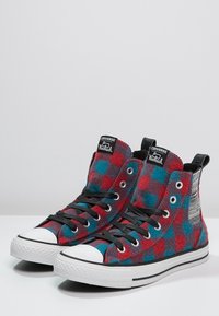 Baskets montantes en flanelle à carreaux rouges et bleus avec des lacets noirs et des semelles en caoutchouc blanches. Présentent un accent textile à motifs à l'arrière.