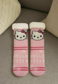 Pair of pink Hello Kitty slippers with white fluffy cuffs resting on a gray couch between beige textured pillows.