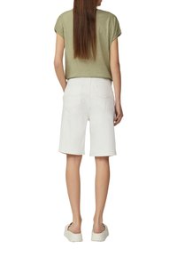 Shorts en denim blanc avec une coupe décontractée, poches arrière et ourlets roulés, associés à un haut à manches courtes vert olive clair. Chaussures plates.