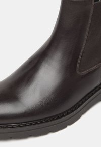 Stivaletto in pelle marrone con finitura lucida, dettagli laterali elasticizzati e suola in gomma con un motivo di battistrada testurizzato.