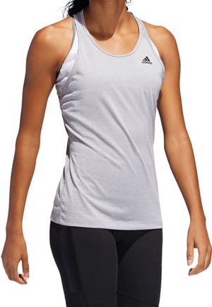 Kobieta ubrana w jasnoszary bezrękawnik sportowy Adidas i czarne legginsy, stojąca z ramionami swobodnie opuszczonymi wzdłuż ciała.