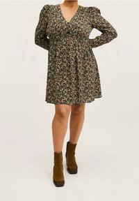 Robe fleurie noire avec un col en V, des manches bouffantes et une taille cintrée. Elle présente un motif floral coloré et une jupe fluide. Bottines marron.