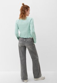 Mintgroene langemouwtop met een geribbelde textuur en een golvende zoom, gecombineerd met hoog-waist grijze breedpijpenjeans en witte sneakers.