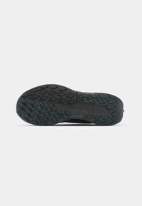 Czarna podeszwa sportowego buta z teksturowaną powierzchnią, na której widoczny jest wzór diamentowy. Zawiera wyraźnie umieszczone logo Nike Trail.
