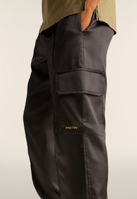 Pantaloni cargo neri realizzati in un materiale liscio e lucido. Include due tasche laterali e il logo dorato "FREDDY" sulla coscia.