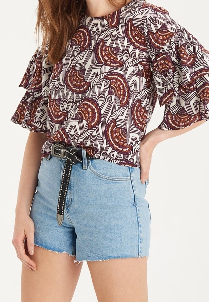 Chemise à manches courtes avec un motif bordeaux et blanc, associée à un short en denim bleu clair avec un ourlet effiloché et une ceinture noire cloutée.