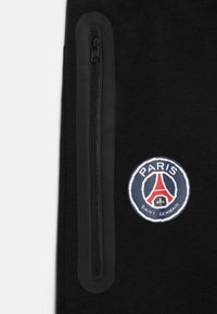 Tessuto nero con una tasca con zip verticale sul lato, caratterizzata da un logo circolare con "Paris Saint-Germain" e un design della Torre Eiffel.