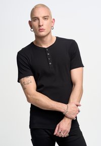 Černé tričko s krátkým rukávem a kulatým výstřihem, s pěti knoflíky; má žebrovanou texturu a přiléhavý střih.