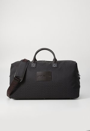 Sac de sport noir en tissu texturé, avec des poignées en cuir et une sangle amovible. Équipé d'un patch logo en relief et d'une fermeture éclair.
