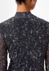 Maglietta sportiva a maniche lunghe con base nera e un motivo astratto viola e bianco. Tessuto liscio e elasticizzato con etichetta visibile sul retro.