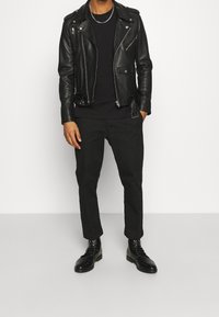 Chaqueta de moto de cuero negro con cremalleras, camiseta negra, pantalones negros y botas negras con cordones. Diseño minimalista, textura elegante.