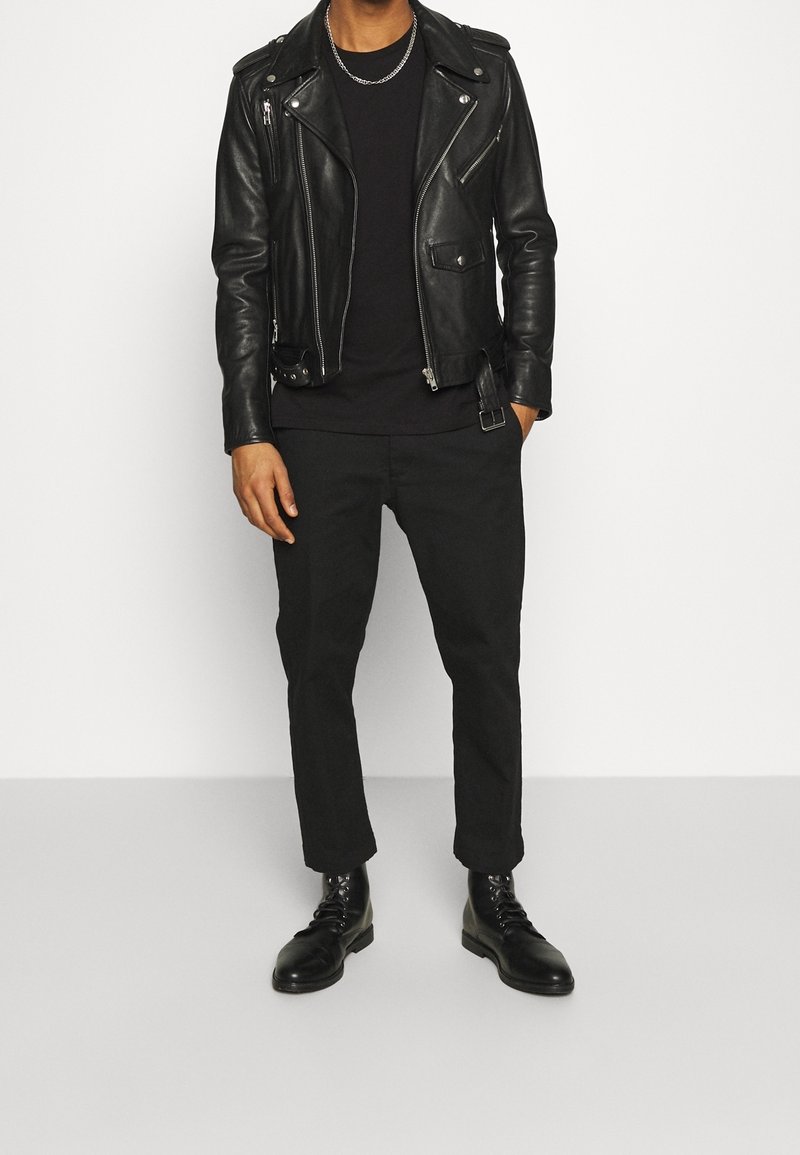 Chaqueta de moto de cuero negro con cremalleras, camiseta negra, pantalones negros y botas negras con cordones. Diseño minimalista, textura elegante.