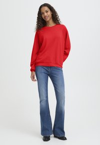 Rode sweatshirt met ronde hals, lange mouwen en subtiel patroon, gecombineerd met flared blauwe jeans en zwarte enkellaarsjes.