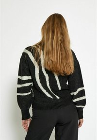 Schwarzer Pullover mit weißen, zebraähnlichen Streifen. Mit gerippten Bündchen und Saum. Stricktextur. Rückansicht zeigt lange, gerade Haare.