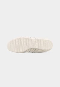 Σόλα μπεζ αθλητικού παπουτσιού Adidas με σχέδιο τρακτερωτού μοτίβου ψαροκόκαλου και με το λογότυπο Adidas ορατό στο κέντρο.