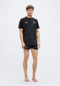 Μαύρο αθλητικό μπλουζάκι με υφή και χρυσές λεπτομέρειες. Συνδυάζεται με μαύρο σορτς που έχει διακριτικό λογότυπο.