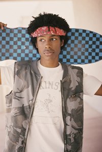 Kameele mustriga vest valge t-särgi peal, millel on graafiline kujundus, hoides sinist ja musta ruuduline rula.