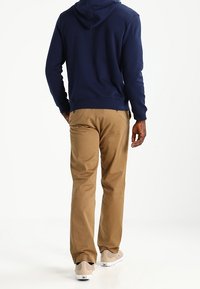 Sweat à capuche bleu marine à coupe décontractée associé à un pantalon chino marron clair, présentant une texture lisse et un léger rétrécissement aux chevilles.