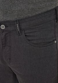 Black denim jeans with a textured, woven surface. Features include a front pocket, metal button fly, and stitched detailing along the seams.