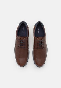 Brown leather shoes with a textured finish, lace-up design, and blue accents at the collar. White stitching along the sole adds detail.