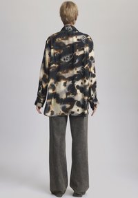 Camicia a maniche lunghe con un motivo astratto in nero, crema e marrone; tessuto in satin liscio; vestibilità morbida; abbinata a pantaloni grigi a gamba larga.