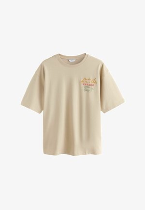 Bézs színű, kerek nyakú, rövid ujjú póló, jobb oldalon kis grafika és "Amor e Vida NAZARE" felirat található.