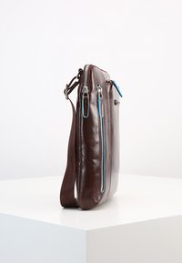 Borsa a tracolla in pelle marrone con un design elegante, caratterizzata da dettagli in zip blu, una tasca con zip sulla parte anteriore e una tracolla texturizzata.