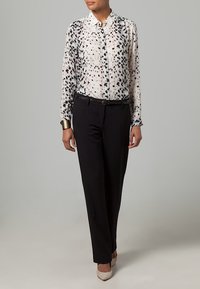 Kevyt, läpikuultava pusero, jossa mustavalkoinen täplikkäät kuvio, kaulus, napitettu, yhdistetty mustiin housuihin ja korkokenkiin.