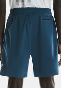 Blue athletic shorts featuring a stretchy waistband, side pockets, and a small zippered pocket on the back. Smooth fabric with a logo.