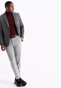 Blazer grigio a quadri sopra un dolcevita borgogna, abbinato a pantaloni grigi chiari e scarpe eleganti nere. Presenta un tessuto strutturato e un design elegante.
