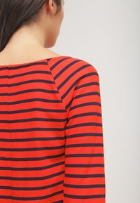 Pull rayé rouge et marine, montrant l'arrière et la zone des épaules, avec un col bateau et un tissu doux et texturé.