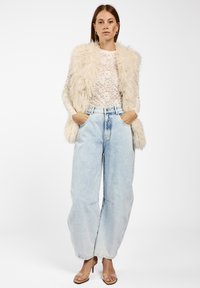 Nepbont vest in roomkleur over een witte kanten top, gecombineerd met lichtblauwe baggy jeans en beige hak sandalen. Duidelijk gedefinieerde texturen en kleuren.